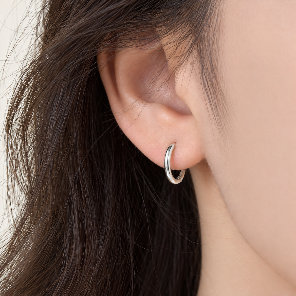 The Kiri Huggie Hoops — Silver huggie — on-ear three-quarter-front view; reference-based AI visualization