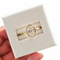 Gold Tone oval moissanite bezel-set ring on an ivory display card, preserved in the original supplier photo angle with white studio surroundings and soft lighting; studio edit and AI enhancement of the existing view.