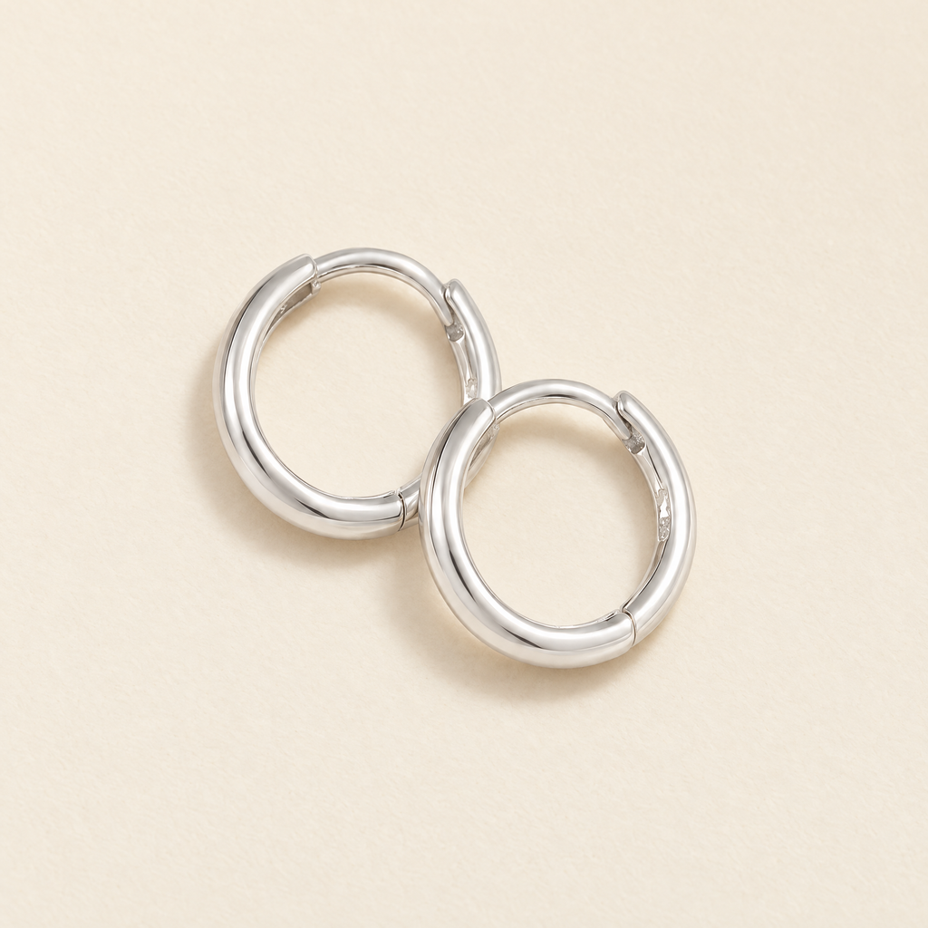The Kiri Huggie Hoops — Silver pair — overlapping cream flat lay; reference-based AI visualization