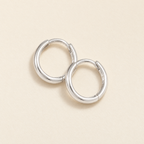 The Kiri Huggie Hoops — Silver pair — overlapping cream flat lay; reference-based AI visualization