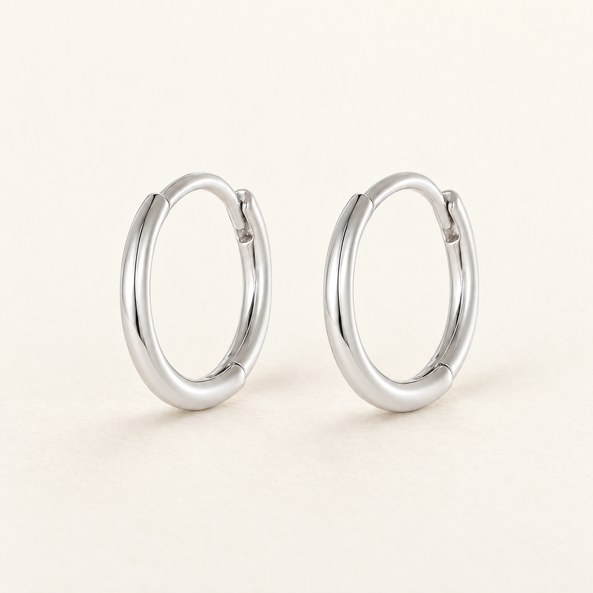 The Kiri Huggie Hoops — Silver pair — closure-focused cream studio view; reference-based AI visualization